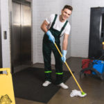 handsome young janitor mopping floor and smiling at camera