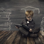 Child Little Boy in Glasses Reading Book over School Black Board